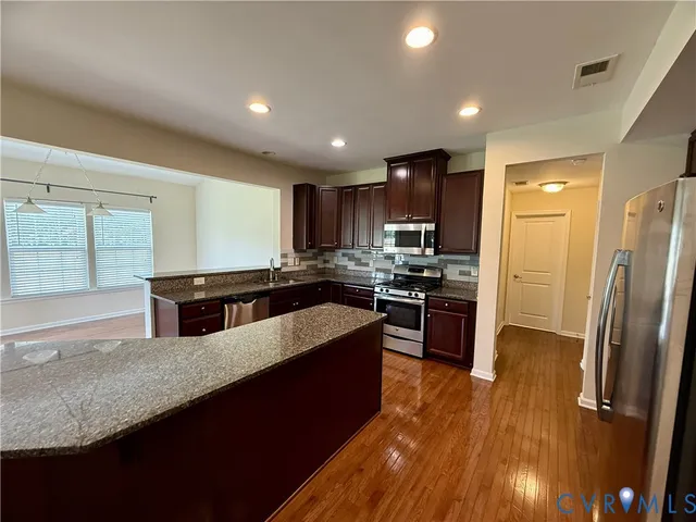 a large kitchen with stainless steel appliances granite countertop a refrigerator a sink dishwasher a stove and white countertops with wooden floor