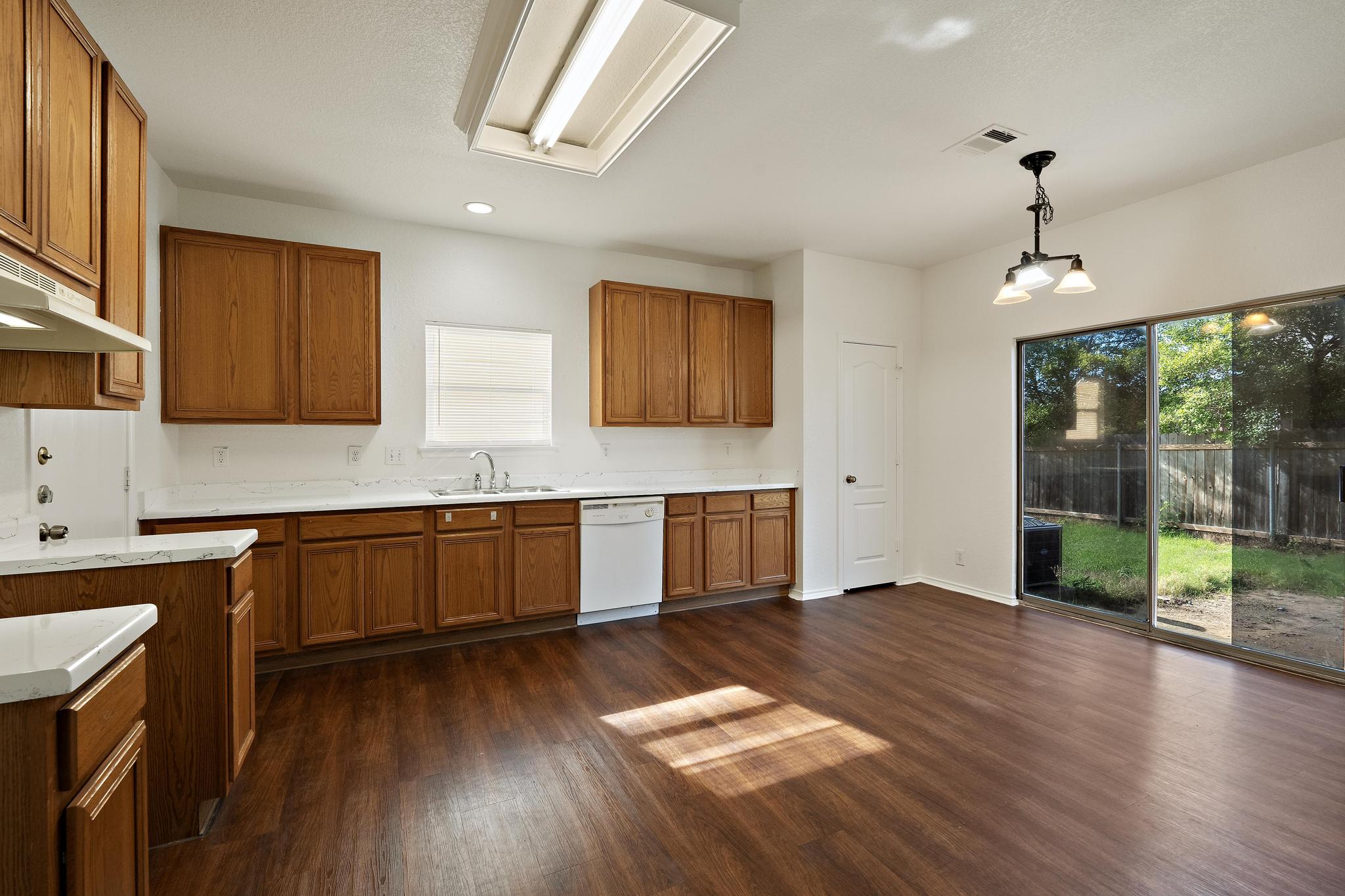 200 Lexington Kyle, TX 78640 - Photo 7 of 25 Kitchen with brown cabinets, light countertops, pendant lighting, dark wood-type flooring, and dishwasher