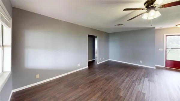 an empty room with wooden floor fan and windows
