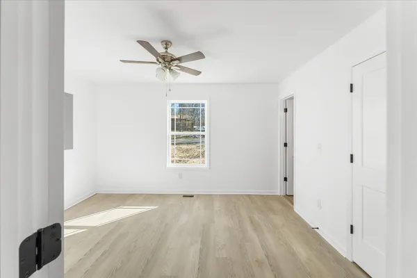 an empty room with wooden floor fan and windows