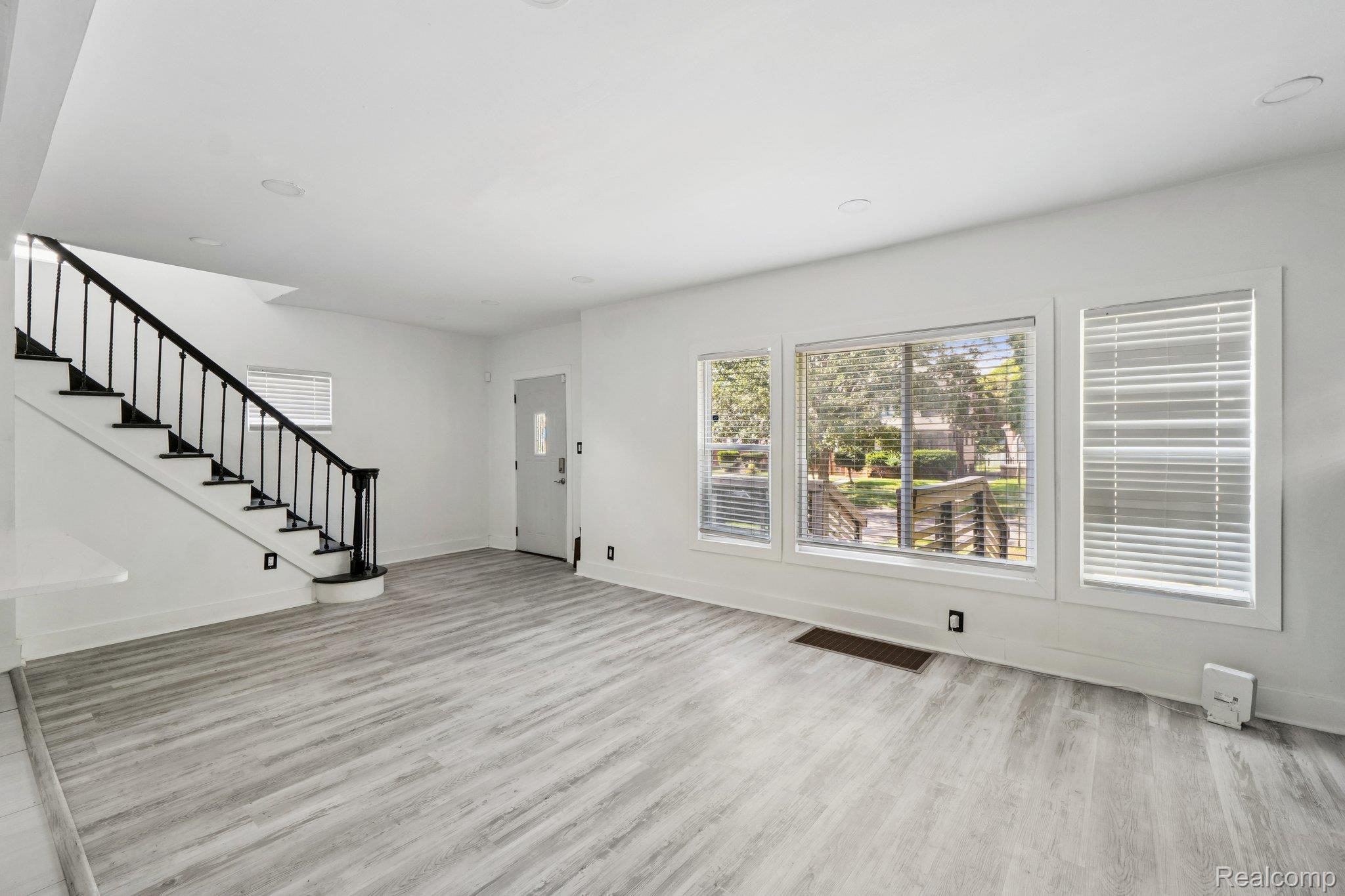 16210 Inverness Street Detroit, MI 48221 - Photo 5 of 29 Light wood-finish flooring, white walls, recessed ceiling lighting, a three-panel window, and a staircase with dark balusters