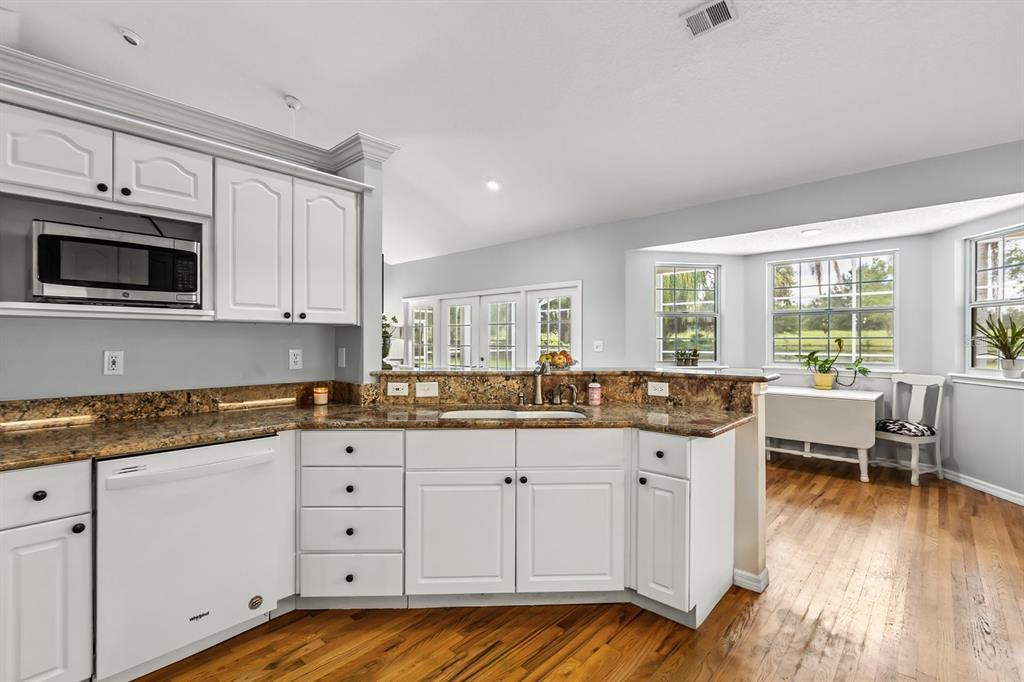 32530 Senese Road Sorrento, FL 32776 - Photo 16 of 34 a kitchen with granite countertop a stove a sink and white cabinets with wooden floor