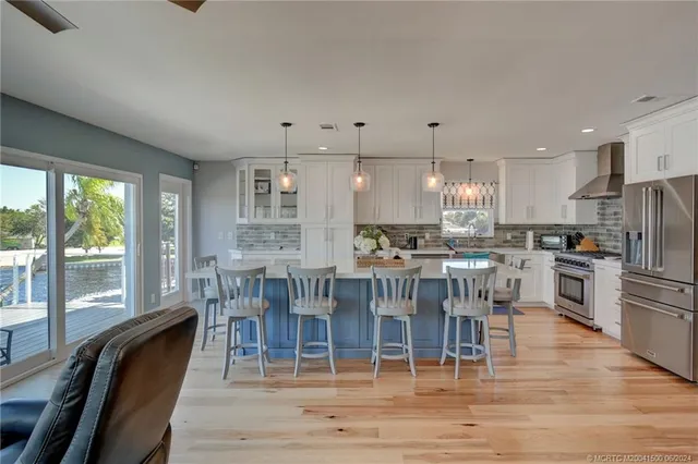 a kitchen with stainless steel appliances granite countertop a stove a refrigerator a kitchen island a dining table and chairs with wooden floor