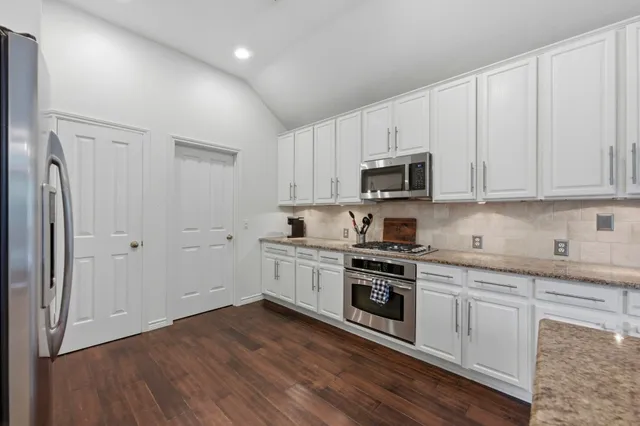 a kitchen with stainless steel appliances granite countertop a stove top oven a sink and white cabinets