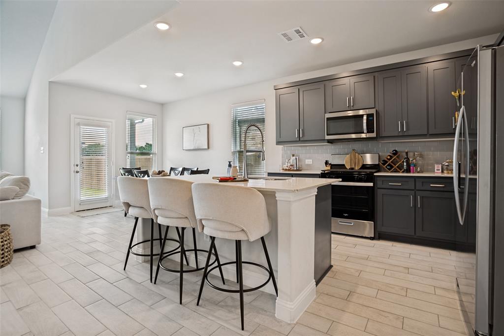 3115 Giovanni Point Princeton, TX 75407 - Photo 9 of 26 Contemporary kitchen featuring dark gray cabinetry, stainless steel appliances, a white subway tile backsplash, and light-toned plank flooring