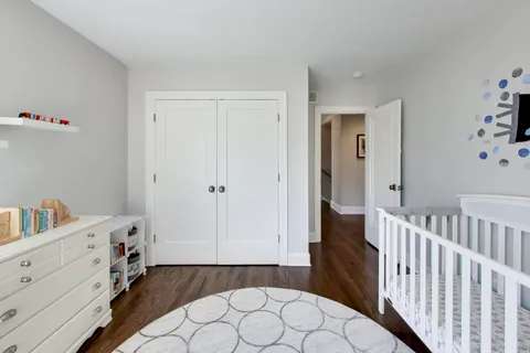 a view of a bedroom with baby crib and wooden floor