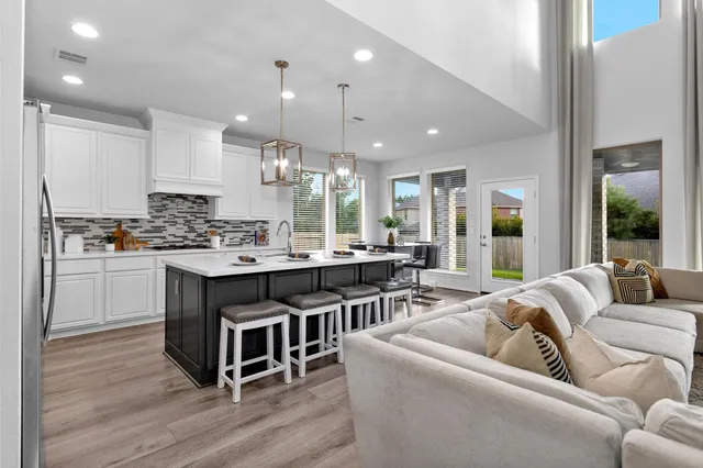 a living room with stainless steel appliances kitchen island granite countertop a couch a stove a sink and a refrigerator with wooden floor