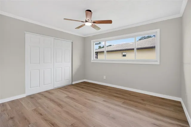 a view of an empty room with wooden floor and a ceiling fan