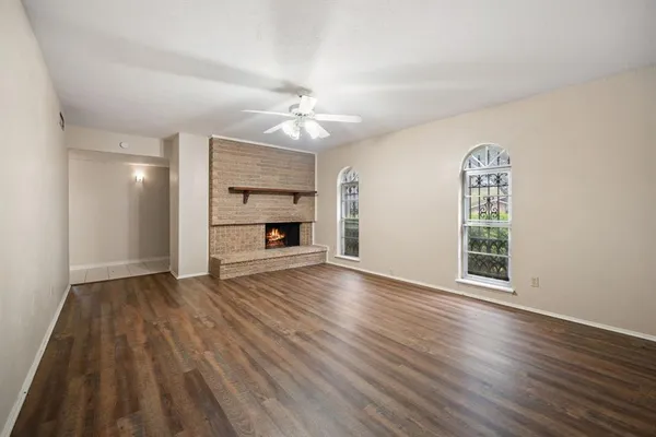an empty room with wooden floor fireplace cabinet and windows