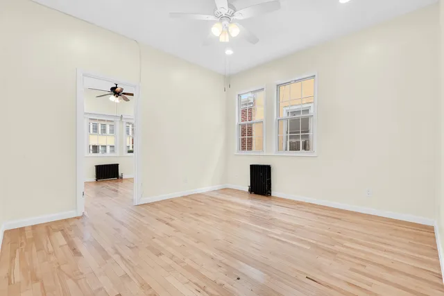 an empty room with wooden floor fan and windows