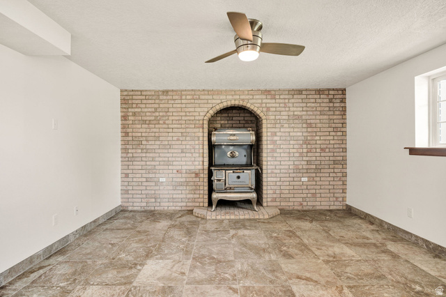365 South Center Street Fielding, UT 84311 - Photo 20 of 41 Unfurnished living room featuring brick wall, a ceiling fan, a wood stove, and a textured ceiling