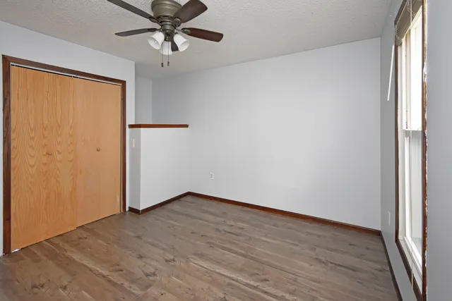an empty room with wooden floor fan and windows