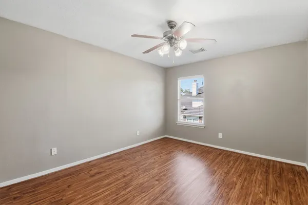 a view of an empty room with wooden floor and a fan