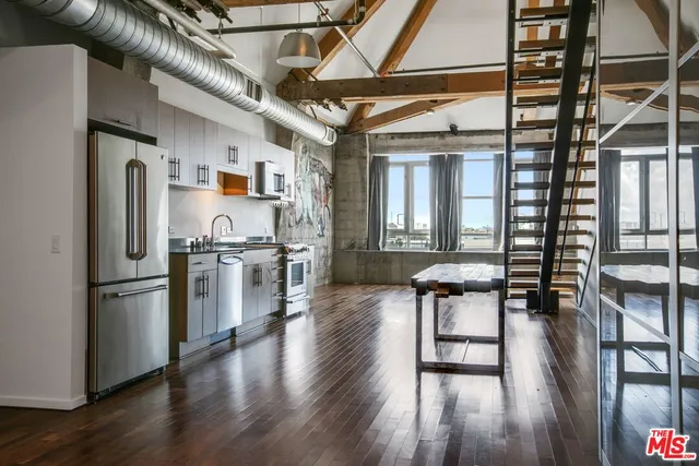 a kitchen with stainless steel appliances granite countertop a refrigerator a microwave oven a stove and a dining table with wooden floors