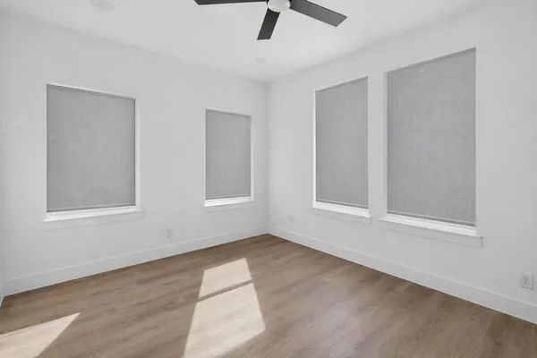 an empty room with wooden floor fan and windows