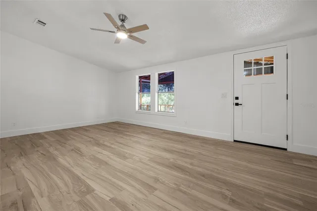 an empty room with wooden floor ceiling fan and windows