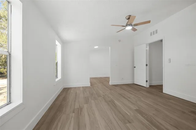 an empty room with wooden floor a ceiling fan and windows