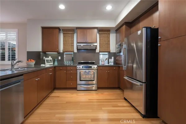 a kitchen with stainless steel appliances granite countertop a refrigerator a stove and a sink with wooden cabinets