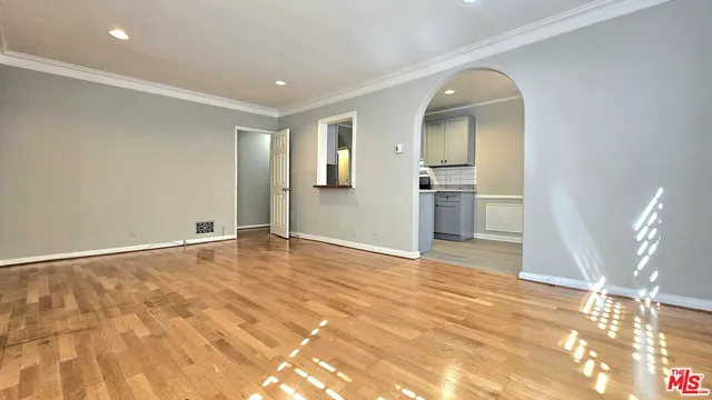 a view of empty room with wooden floor and kitchen view