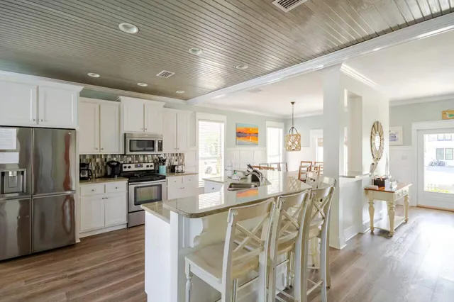 a kitchen with stainless steel appliances kitchen island granite countertop a refrigerator a stove top oven a sink dishwasher a dining table and chairs with wooden floor