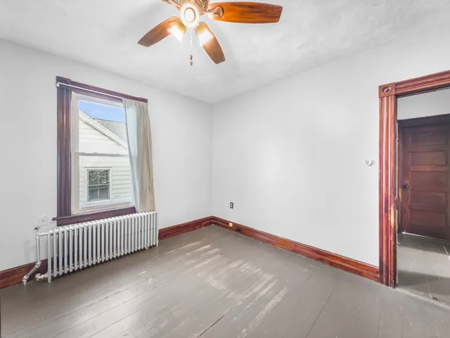 an empty room with chandelier fan and windows