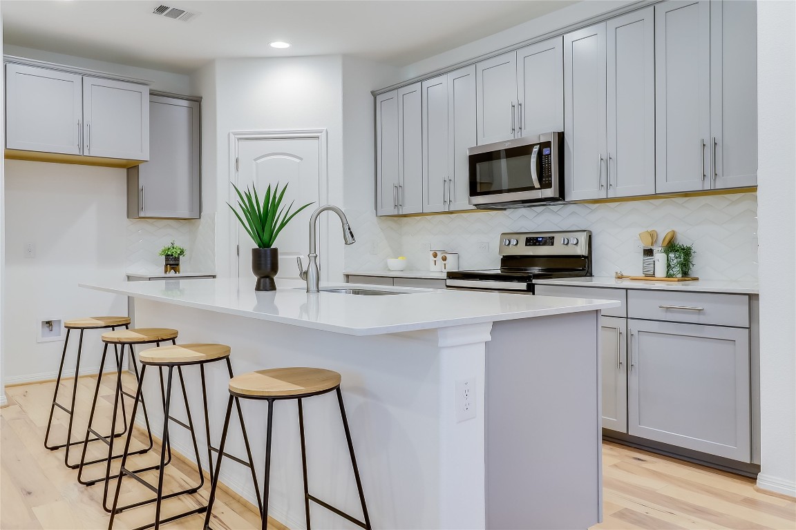 Kitchen with decorative backsplash, light wood-type flooring, stainless steel appliances, a breakfast bar area, and a center island with sink