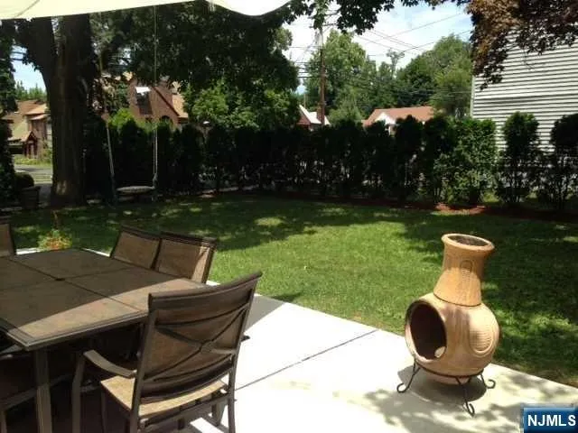 a backyard of a house with table and chairs plants and large trees