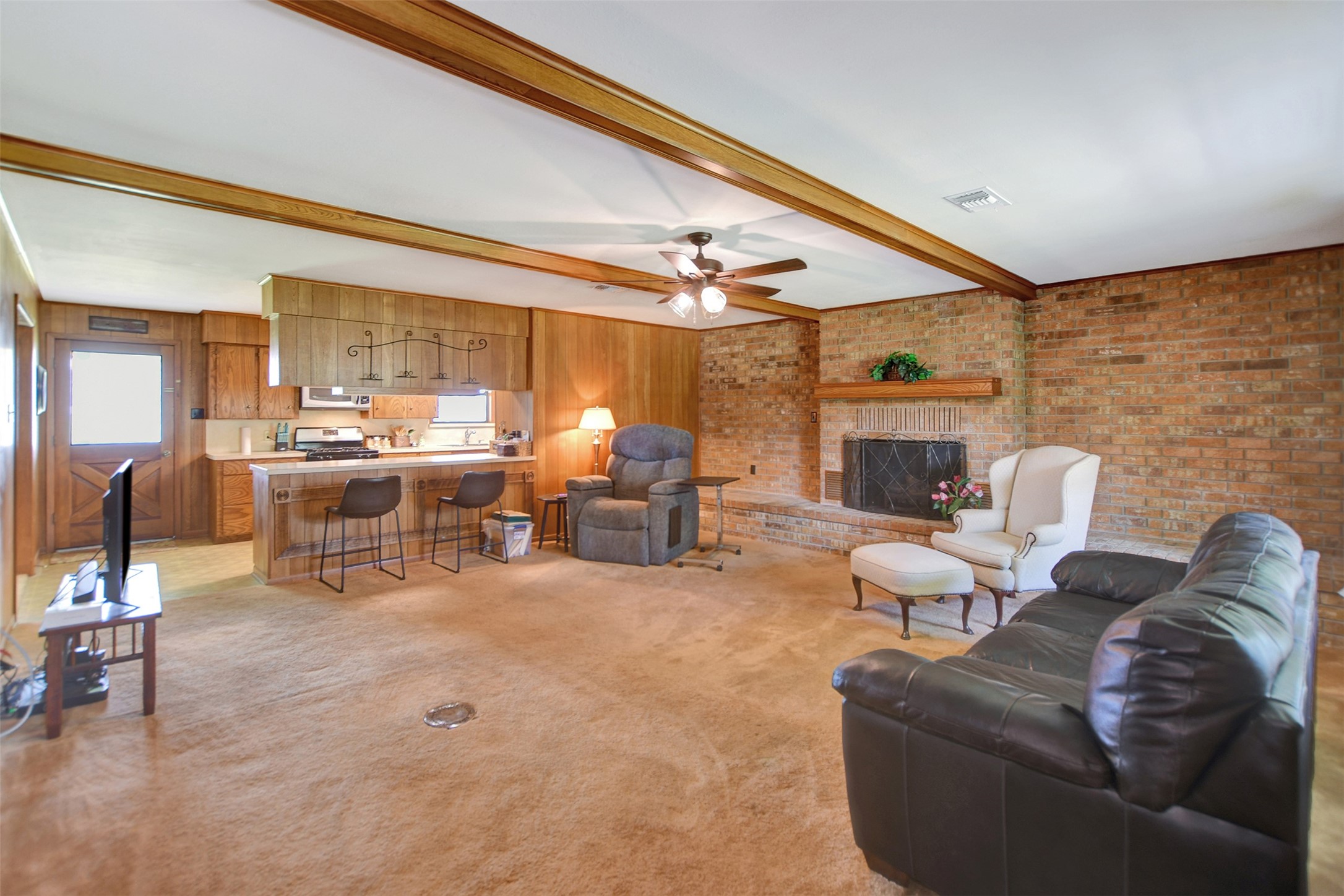 341 South S Loop Bellville, TX 77418 - Photo 6 of 33 This spacious living area features a cozy brick fireplace, exposed wooden beams, and an open layout connecting to the kitchen. The room offers ample natural light and comfortable seating, perfect for gatherings.