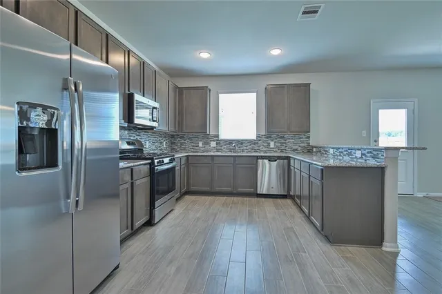 a kitchen with stainless steel appliances granite countertop a stove a sink dishwasher a refrigerator and white cabinets with wooden floor