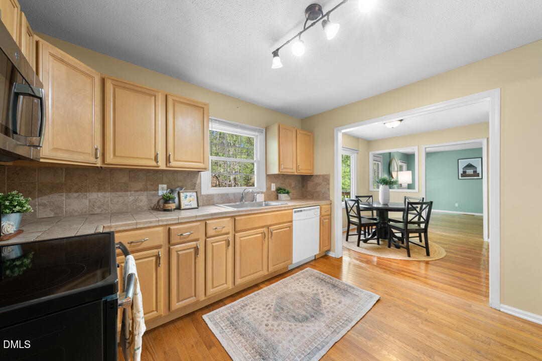 122 Stedwick Place Durham, NC 27712 - Photo 17 of 39 a kitchen with stainless steel appliances granite countertop a stove top oven a sink dishwasher a dining table and chairs with wooden floor