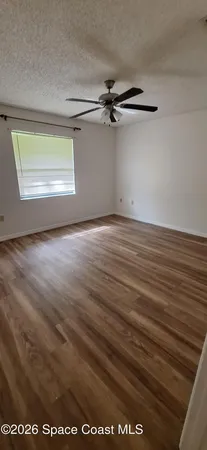 a view of a room with wooden floor a ceiling fan and windows