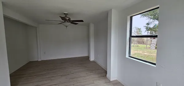 an empty room with wooden floor ceiling fan and windows
