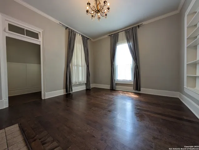 an empty room with wooden floor chandelier and windows