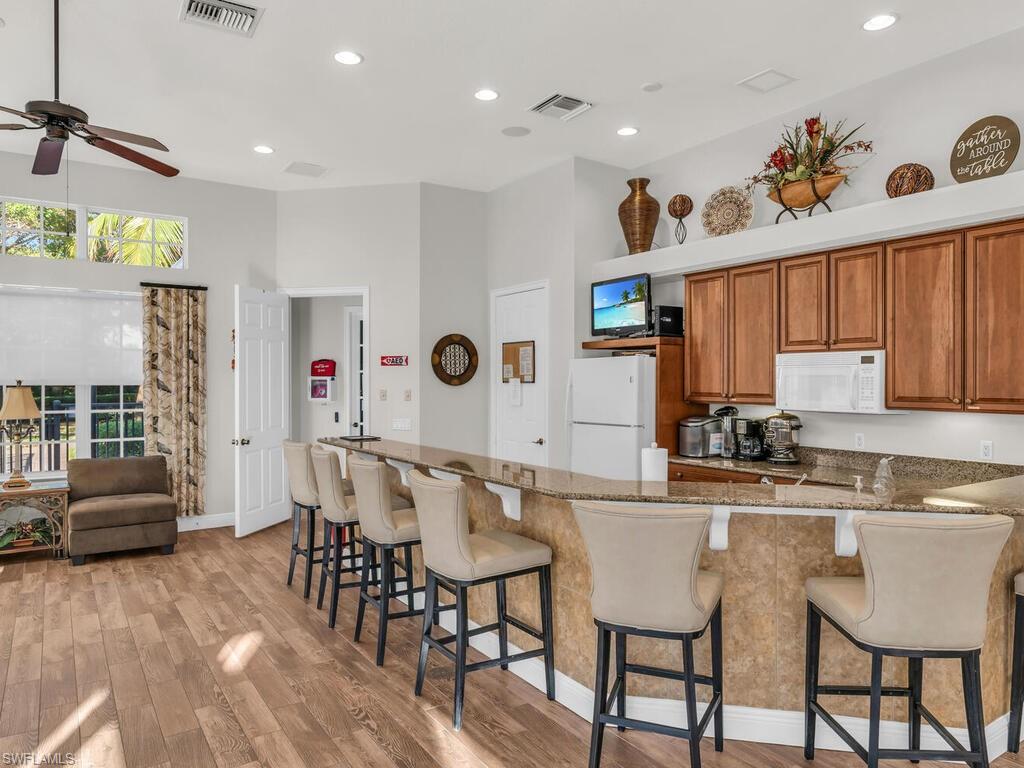 7869 Hawthorne Drive, Unit 303 Naples, FL 34113 - Photo 44 of 50 Kitchen featuring white appliances, ceiling fan, stone countertops, light hardwood / wood-style floors, and a breakfast bar area