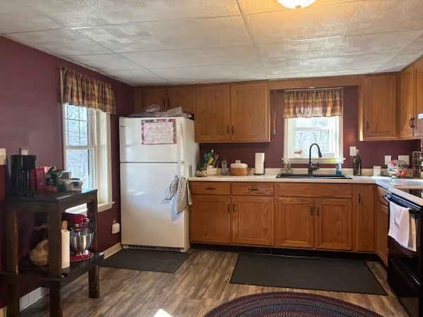 a kitchen with granite countertop a refrigerator a sink dishwasher a stove and white countertops with wooden floor