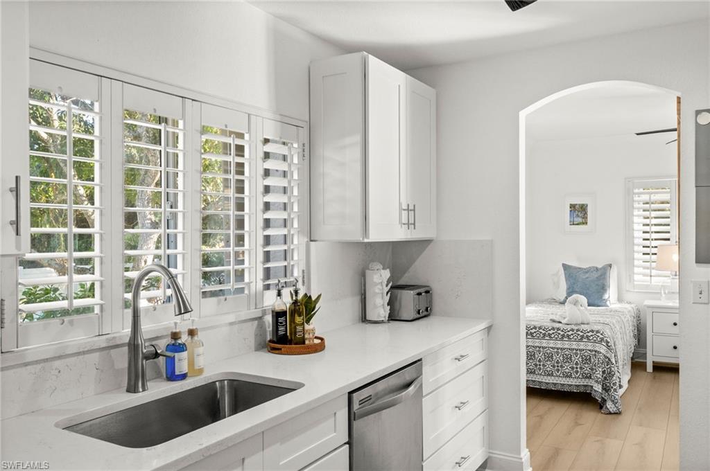 4 Colonial Drive Naples, FL 34112 - Photo 8 of 42 Kitchen featuring white cabinetry, stainless steel dishwasher, light stone countertops, light wood-style flooring, and arched walkways