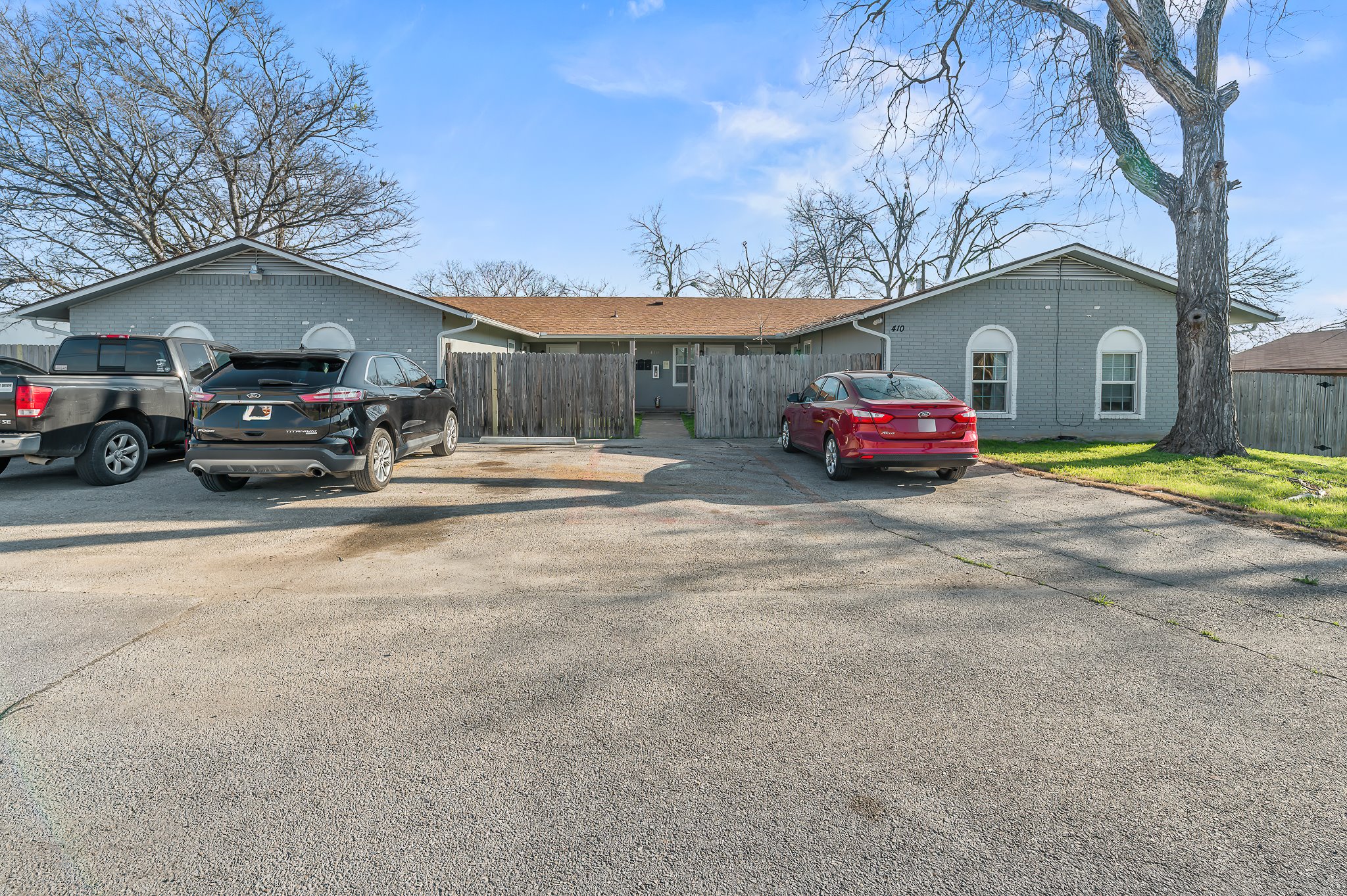 Exterior featuring a pitched roof, light-colored siding, arched windows, and a paved parking area