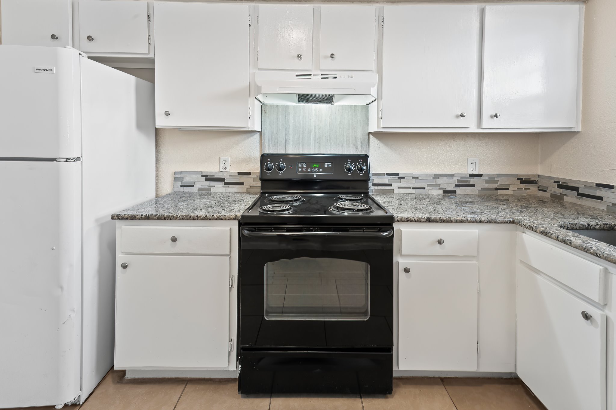 410 Old Thorndale Road, Unit D Taylor, TX 76574 - Photo 8 of 14 Modern kitchen featuring white cabinetry, granite-style countertops, mosaic tile backsplash, and a black electric range with an overhead vent