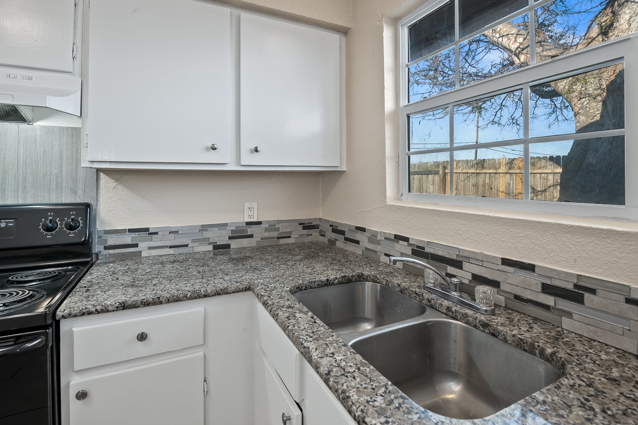 410 Old Thorndale Road, Unit D Taylor, TX 76574 - Photo 9 of 14 Kitchen area featuring white cabinetry, a black electric range, a stainless steel double basin sink, and a multi-tone tile backsplash