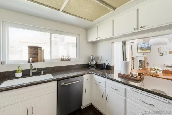a kitchen with granite countertop a sink stainless steel appliances white cabinets and a window