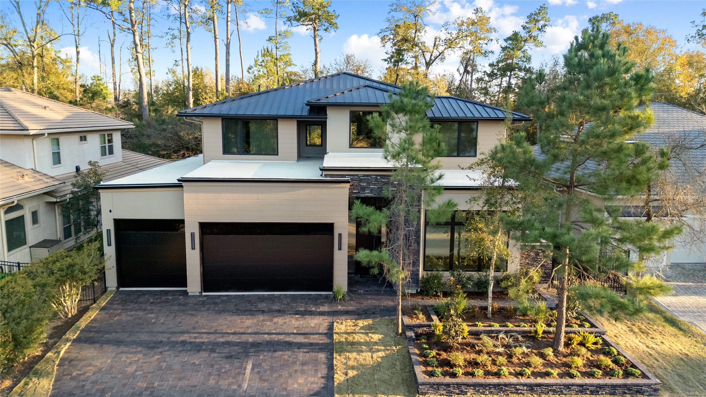 47 Pronghorn Place Spring, TX 77389 - Photo 1 of 48 Modern two-story home with a sleek facade, featuring large windows and a dark roof. It includes a spacious driveway leading to a three-car garage. The front yard is landscaped with trees and shrubs, offering a serene setting surrounded by a wooded backdrop.