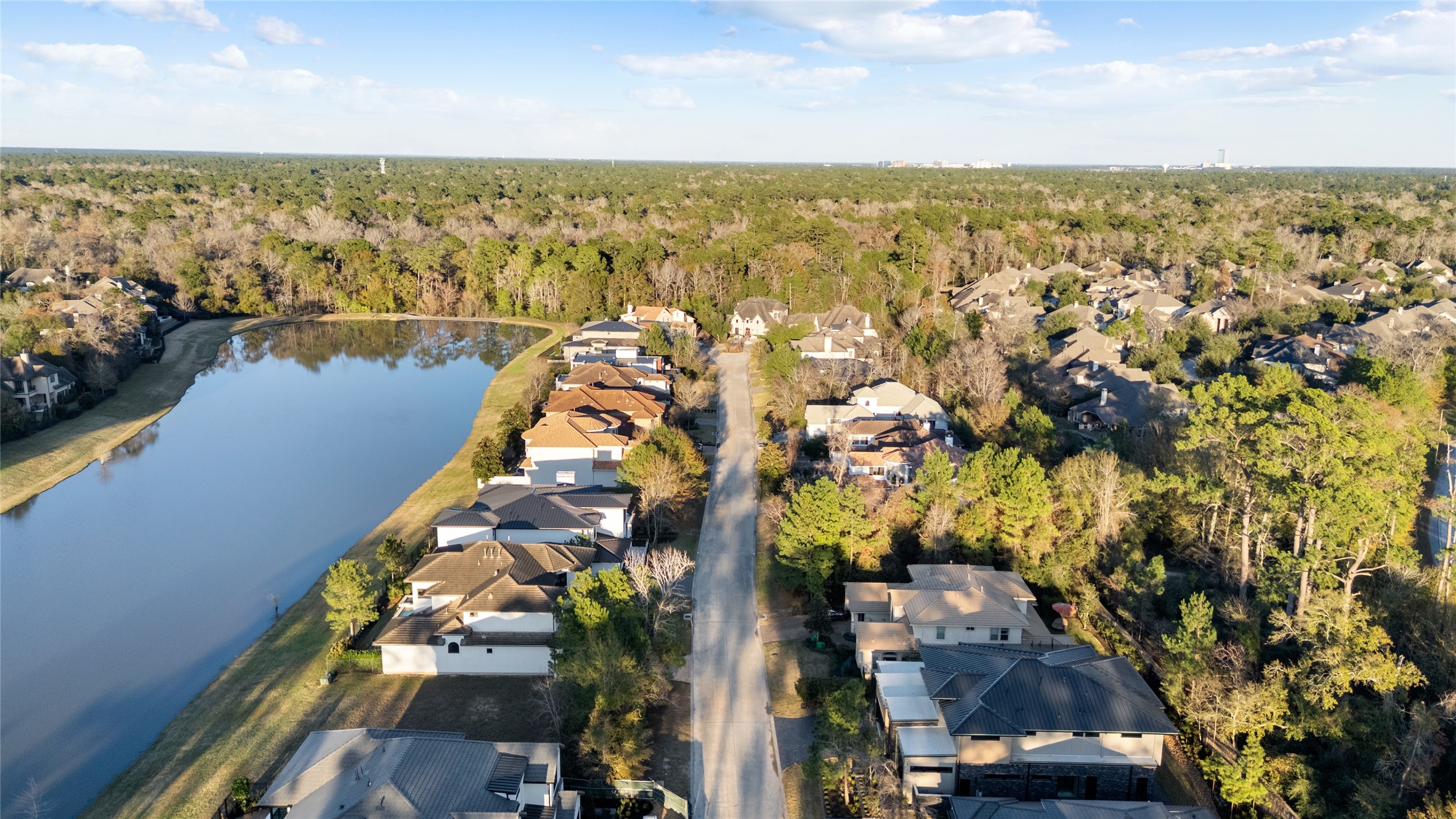 47 Pronghorn Place Spring, TX 77389 - Photo 2 of 48 This aerial view showcases a serene residential neighborhood nestled beside a tranquil lake, surrounded by lush greenery and trees, offering a peaceful and picturesque setting for potential homebuyers.