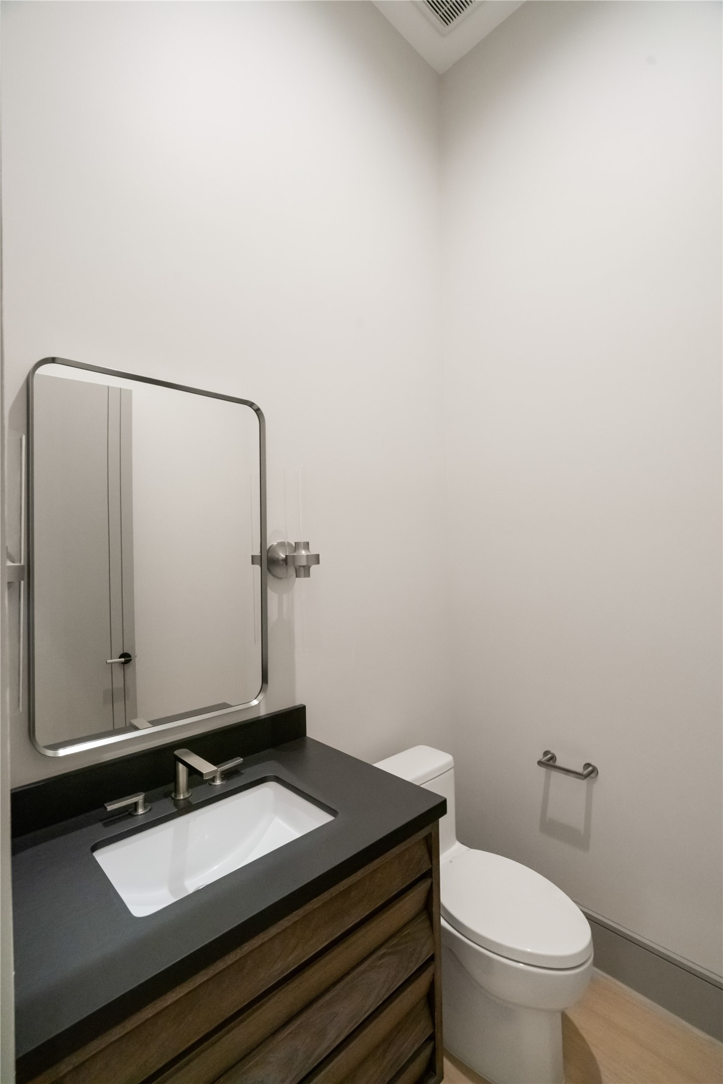 47 Pronghorn Place Spring, TX 77389 - Photo 41 of 48 This photo shows a modern, compact bathroom with a minimalist design. It features a sleek vanity with a dark countertop, a rectangular mirror, and a standard toilet. The walls are light-colored, enhancing the room's brightness and simplicity.