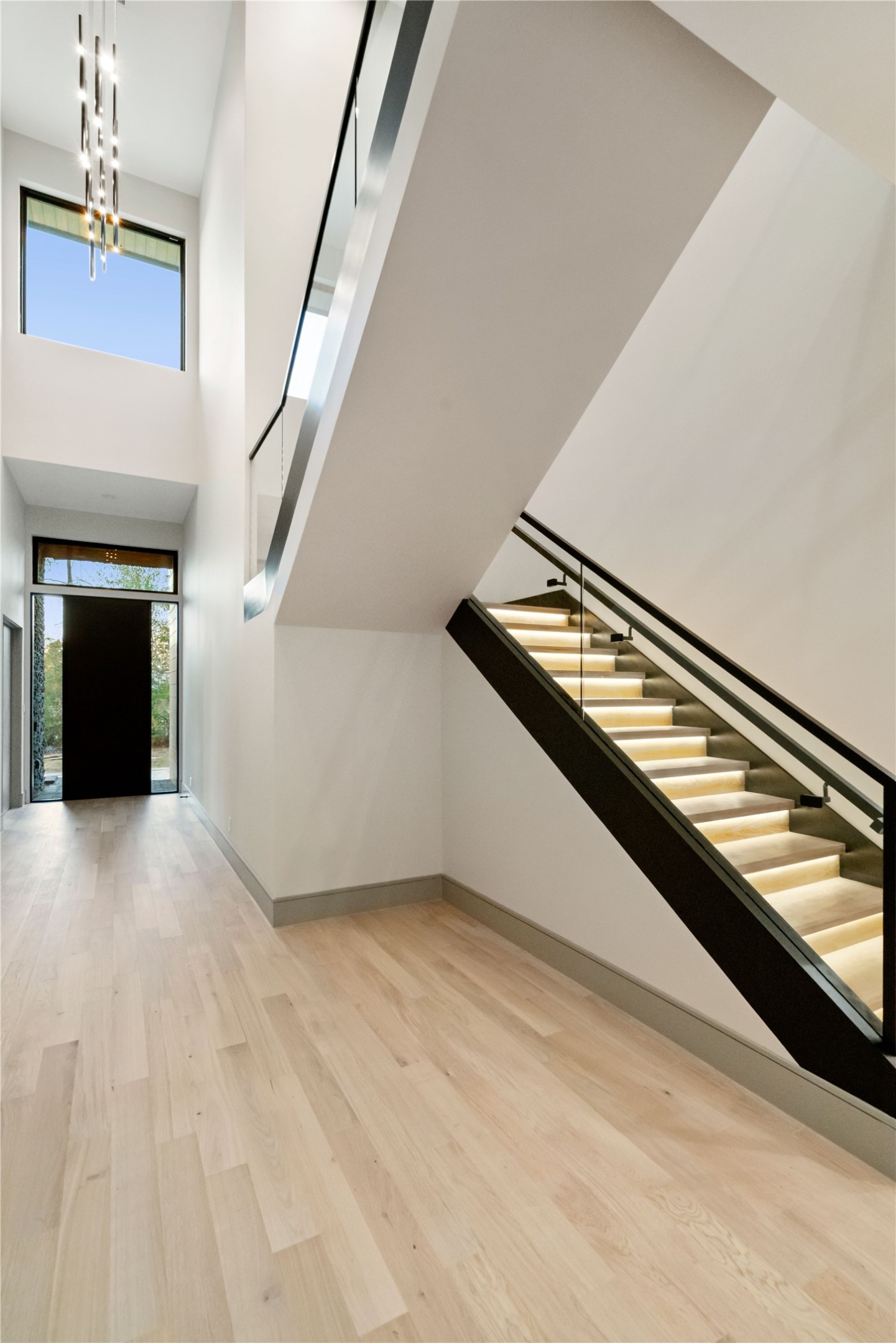 47 Pronghorn Place Spring, TX 77389 - Photo 8 of 48 This modern entryway features high ceilings, a sleek staircase with under-step lighting, and ample natural light from large windows, creating an inviting and spacious atmosphere.