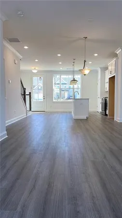 a view of an empty room and kitchen with wooden floor