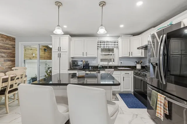 a kitchen with stainless steel appliances kitchen island granite countertop a refrigerator a stove a sink a dining table and chairs with wooden floor