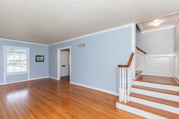 a view of an empty room with wooden floor and stairs