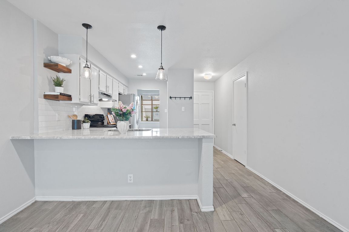 Kitchen with light stone counters, a peninsula, white cabinetry, hanging light fixtures, and light wood-style floors