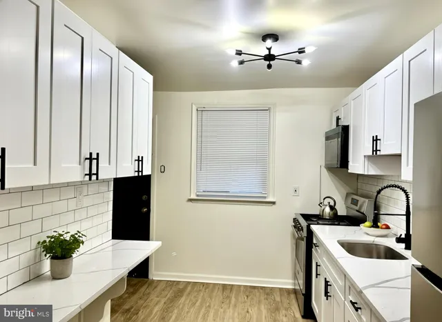 a kitchen with stainless steel appliances sink stove and white cabinets with wooden floor