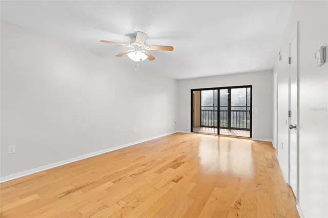 a view of an empty room with wooden floor and fan